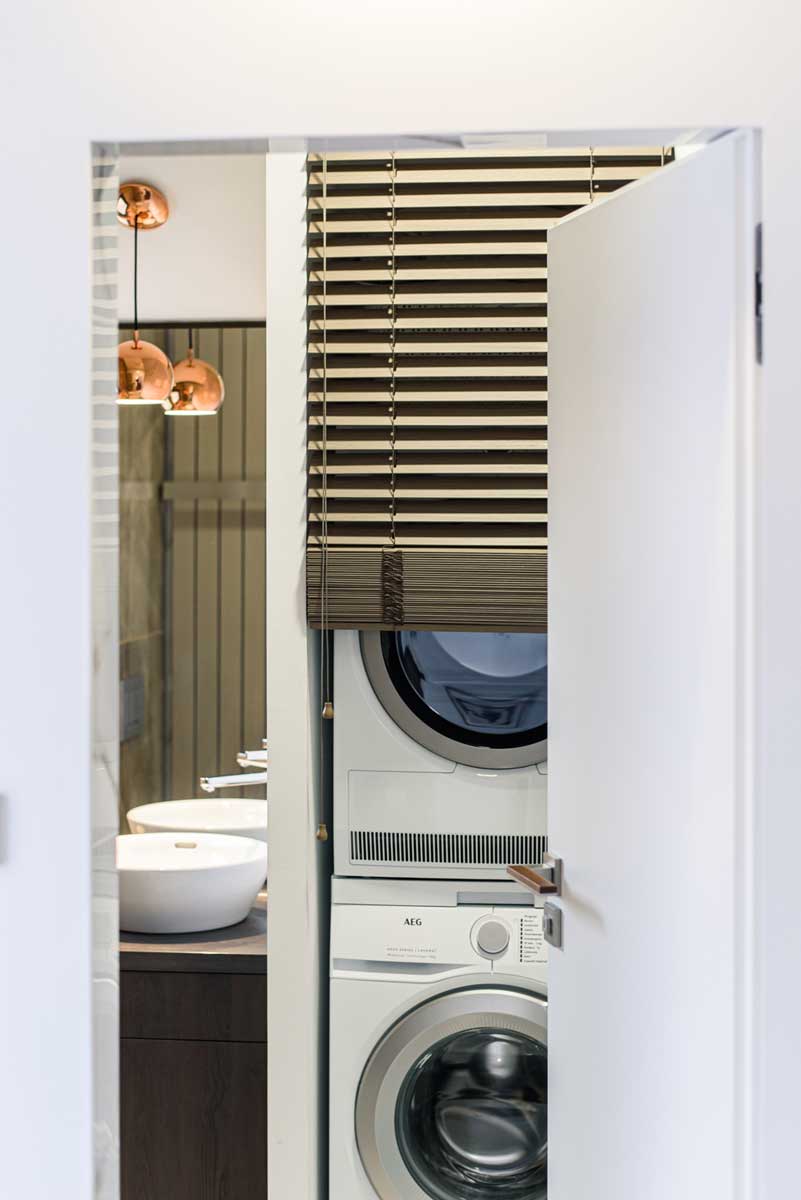 Vestavěná pračka a sušička skryté ve skříni v koupelně s důrazem na čistotu a kompaktní řešení.