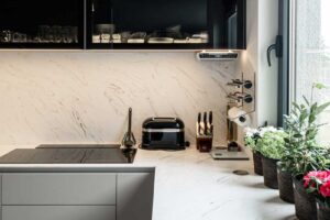 Kuchyňská pracovní deska v mramorovém dekoru s navazujícím obkladem a vestavěnými spotřebiči.