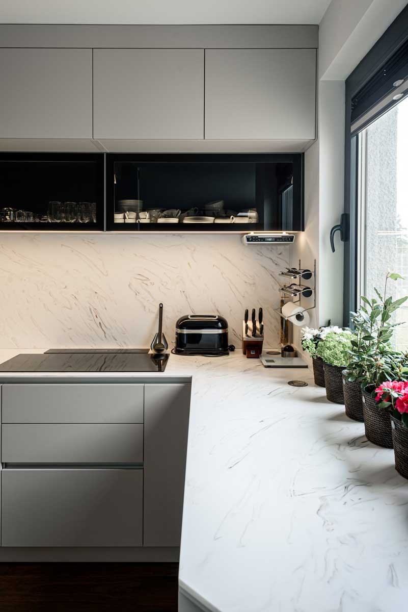 Kuchyňská pracovní deska v mramorovém dekoru s navazujícím obkladem a vestavěnými spotřebiči.