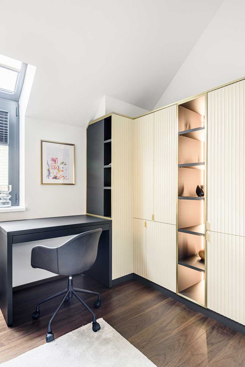 Pracovní kout s vestavěným stolem a vitrínovou skříní s jemným podsvícením.