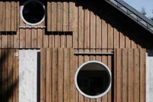 Přední stěna stodoly s dřevěnou fasádou kruhovými okny a betonovými rámy