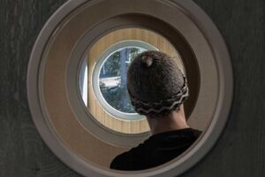 Pohled skrz kruhové okno v interiéru směrem do dřevěné fasády a krajiny