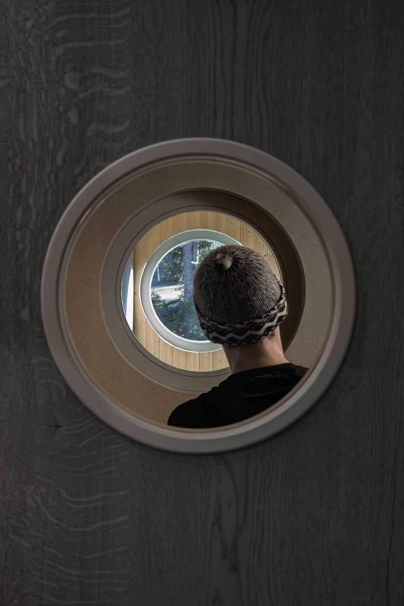 Pohled skrz kruhové okno v interiéru směrem do dřevěné fasády a krajiny