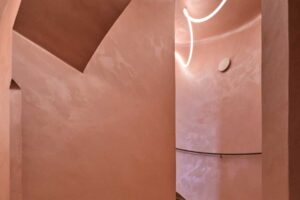 Původní křivočaré schodiště v pavlačovém domě s pudrově tónovanými stěnami a jemným osvětlením