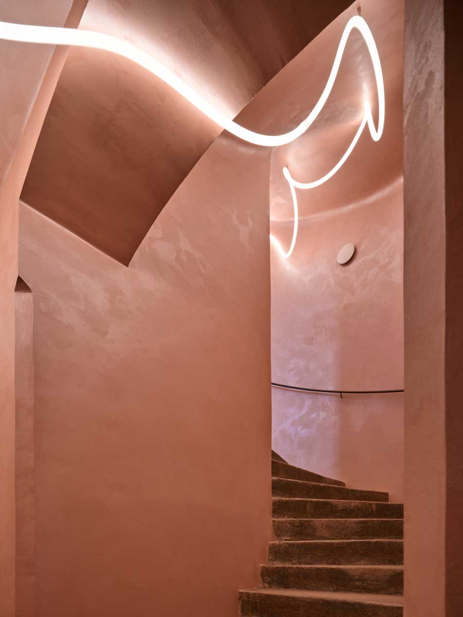 Původní křivočaré schodiště v pavlačovém domě s pudrově tónovanými stěnami a jemným osvětlením