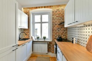 Moderní kuchyně s odhalenou cihlovou zdí a původním obloukem kolem okna propojující historický charakter s čistým designem