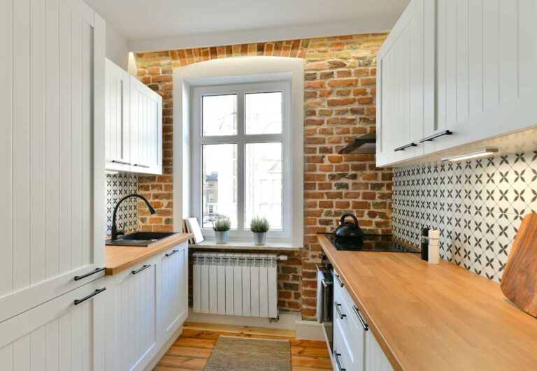 Moderní kuchyně s odhalenou cihlovou zdí a původním obloukem kolem okna propojující historický charakter s čistým designem