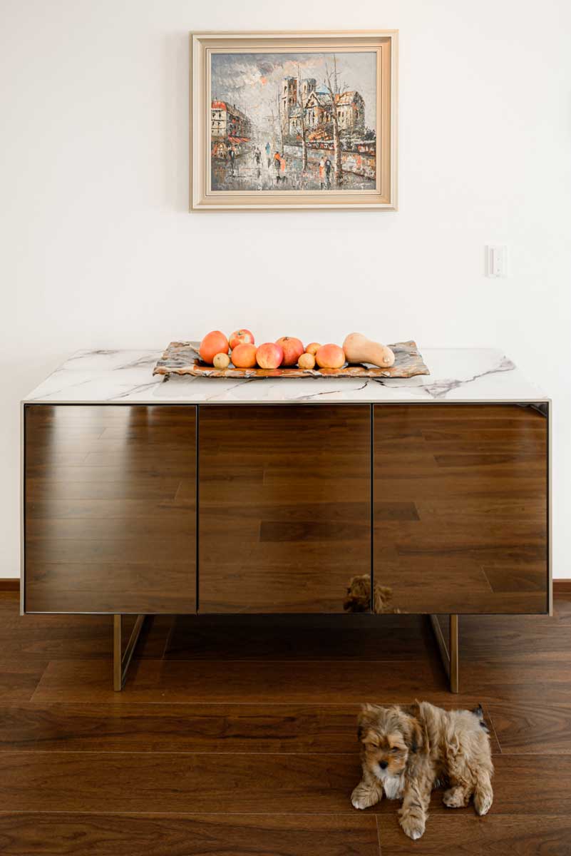 Komoda s lesklými dvířky v dřevěném dekoru a kamennou deskou s dekorací.