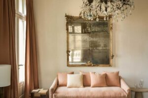 Růžová pohovka v ložnici s historickým zrcadlem a křišťálovým lustrem