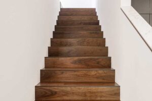 Dřevěné schodiště s masivními nášlapy v tmavém ořechovém odstínu a bílými stěnami.