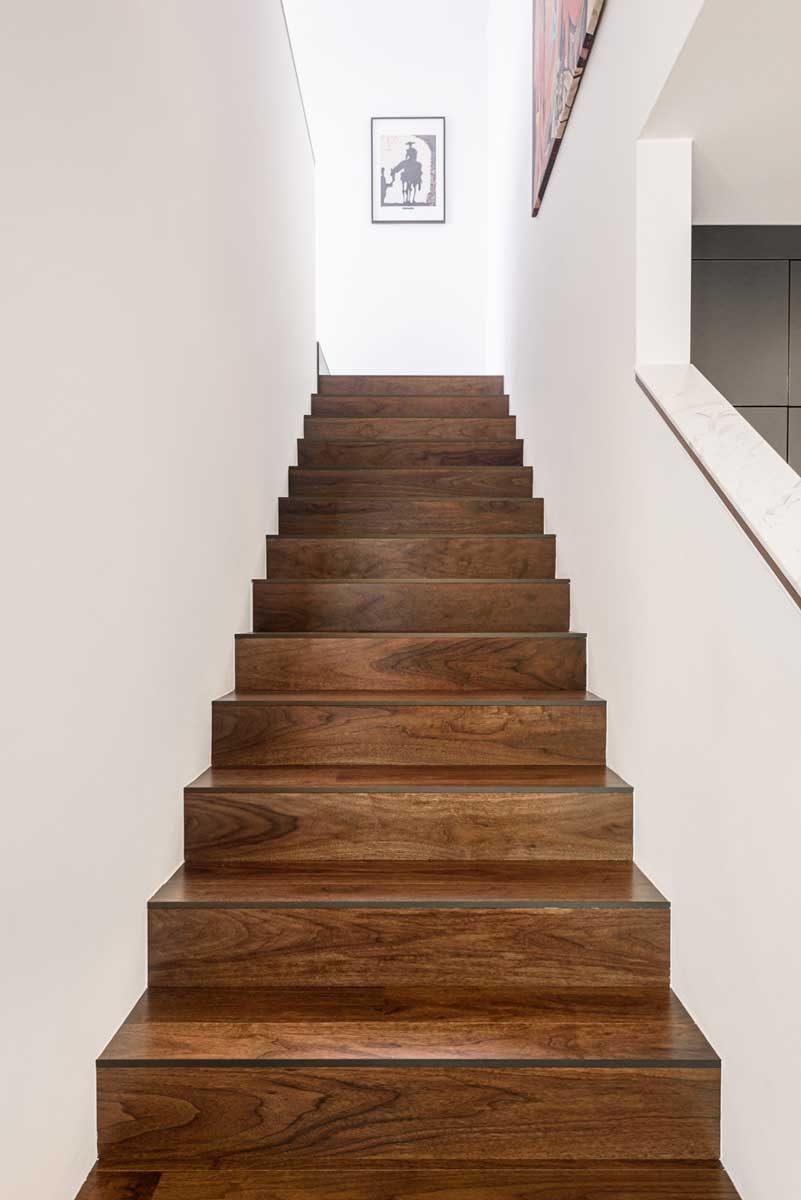 Dřevěné schodiště s masivními nášlapy v tmavém ořechovém odstínu a bílými stěnami.