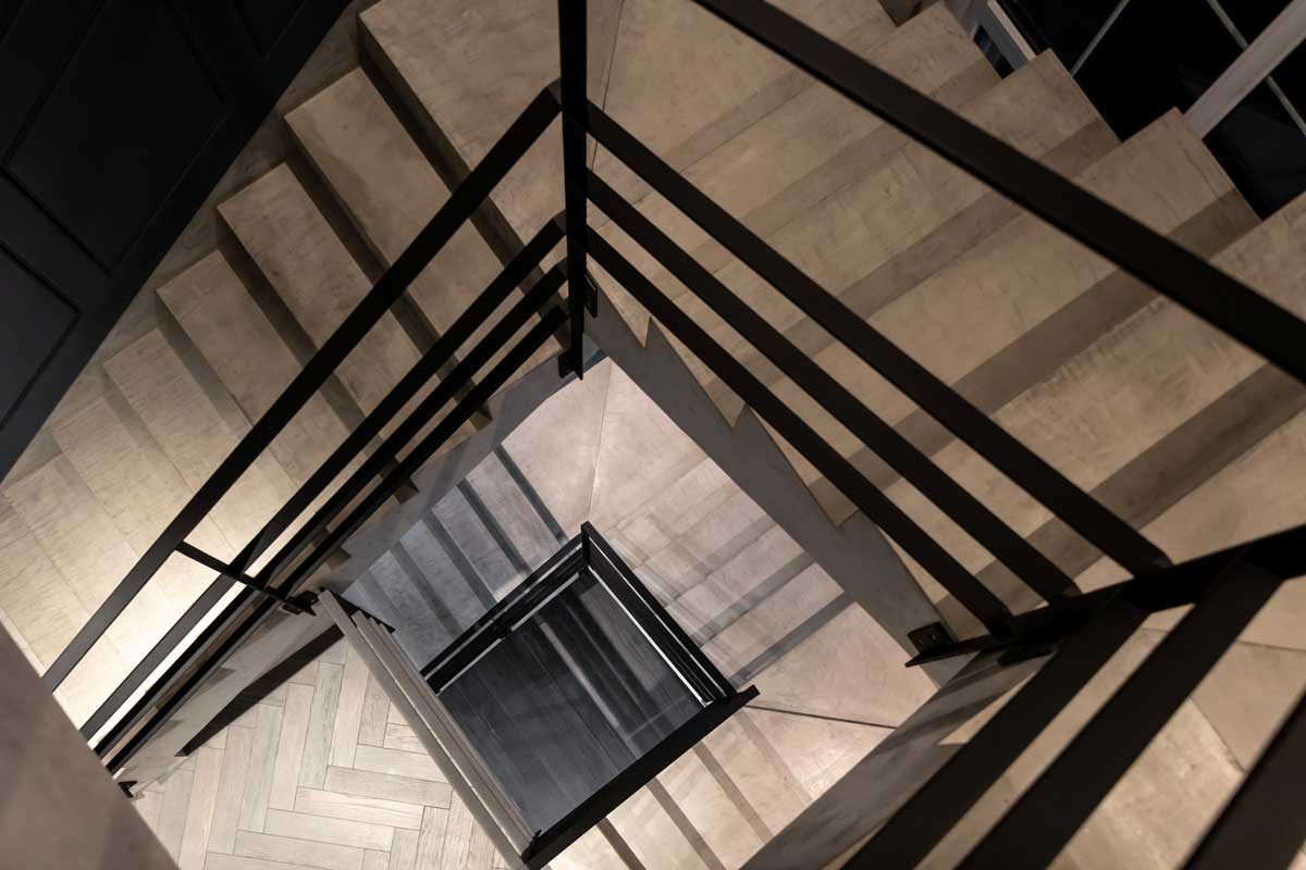 Detail betonového schodiště s černým kovovým zábradlím shora