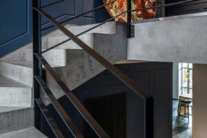 Betonové schodiště s černým kovovým zábradlím a tmavě modrými stěnami