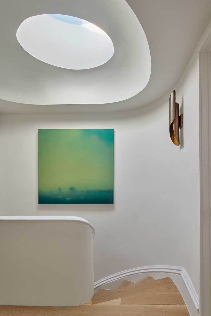 Schodiště s oblými liniemi doplněné obrazem a střešním světlíkem