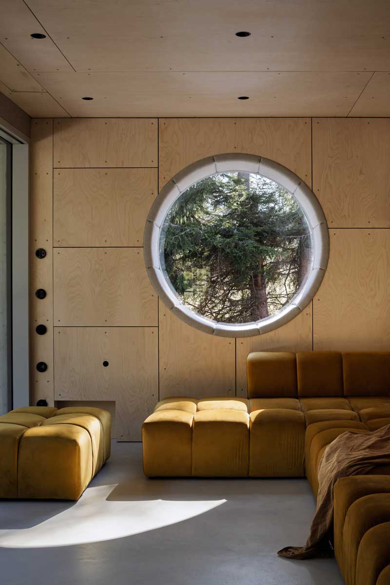 Obývací prostor s modulovou sedačkou kruhovým oknem a dřevěnou vestavbou
