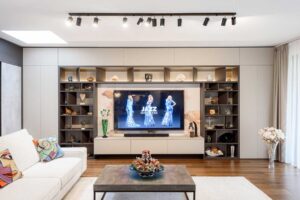 Obývací pokoj se sedací soupravou a televizní stěnou s vestavěnými policemi a dekoracemi.