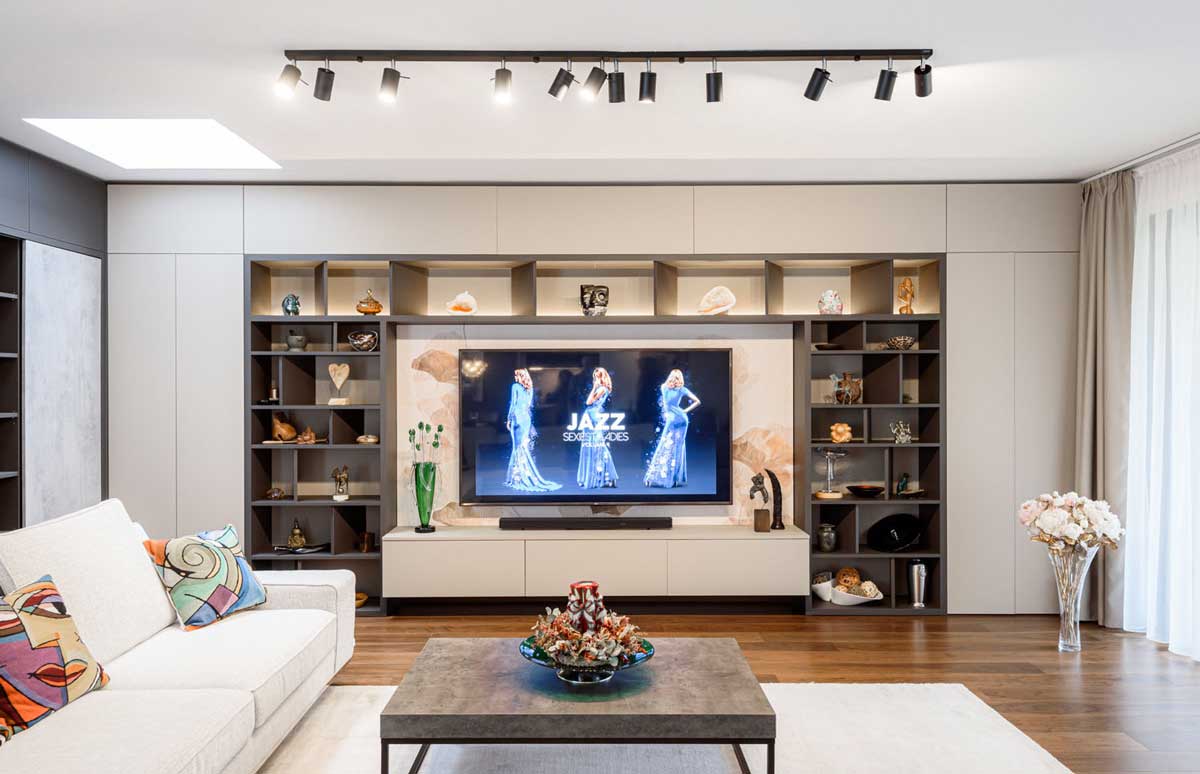 Obývací pokoj se sedací soupravou a televizní stěnou s vestavěnými policemi a dekoracemi.