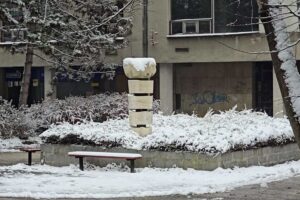 Socha v zimním městském prostoru Orlové doplněná lavičkami a stromy.