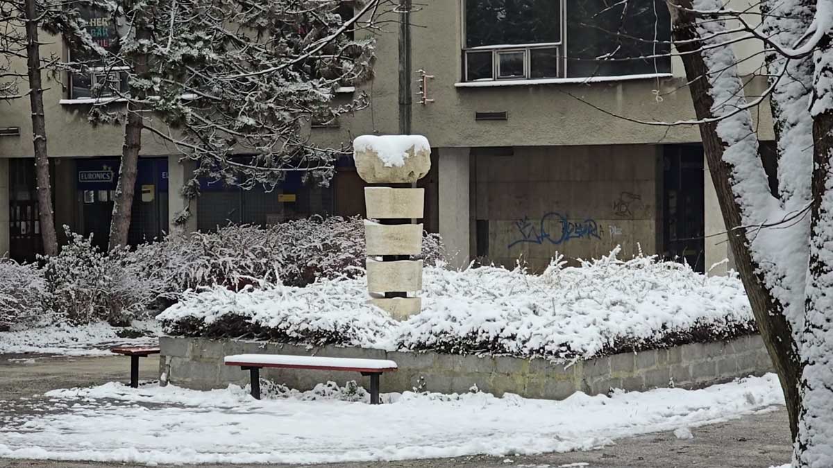 Socha v zimním městském prostoru Orlové doplněná lavičkami a stromy.