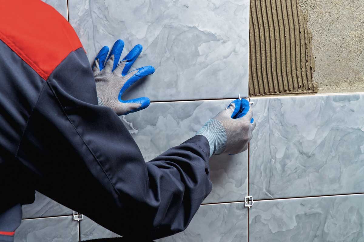 Obkladač vyrovnává dlaždice na stěně pomocí křížků při pokládce obkladu