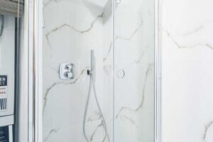 Sprchový kout se skleněnými zástěnami a obkladem v mramorovém dekoru.