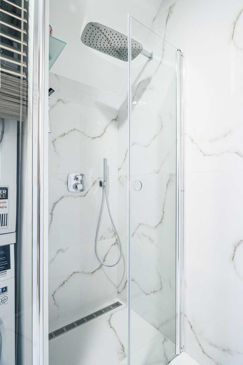 Sprchový kout se skleněnými zástěnami a obkladem v mramorovém dekoru.