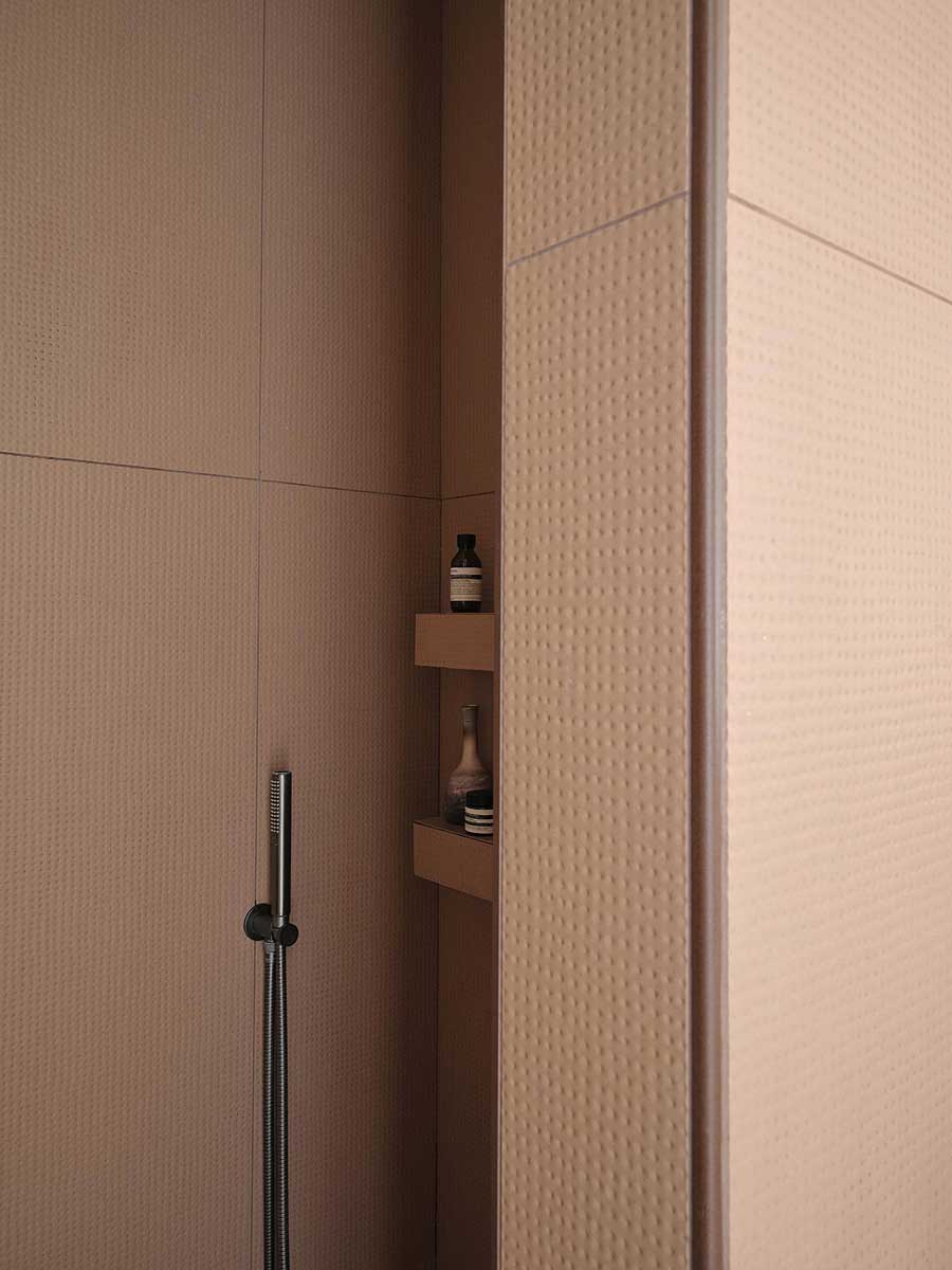 Detail sprchového koutu s keramickým obkladem a integrovanými policemi