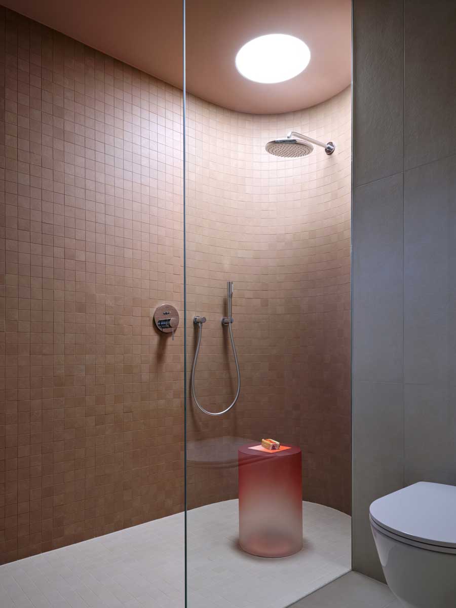 Sprchový kout v moderní koupelně s jemnými tóny a kruhovým světlíkem v rekonstruovaném domě