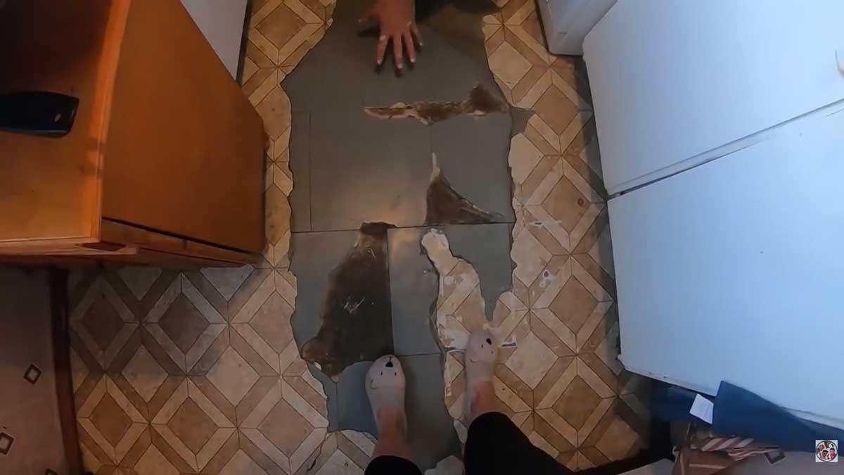 Původní podlaha v kuchyni s poškozenými dlaždicemi a viditelným opotřebením