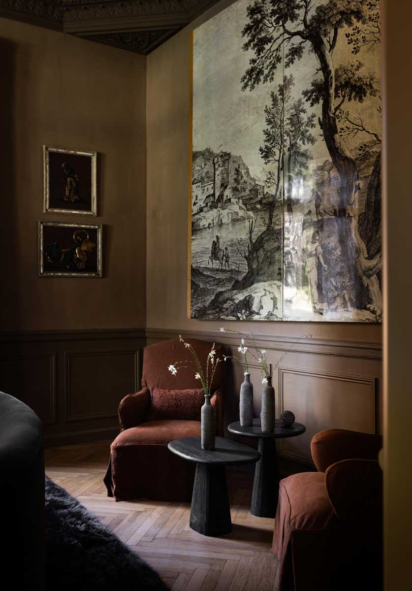 Tmavý společenský kout s čalouněnou pohovkou, historickou tapiserií a křišťálovým lustrem