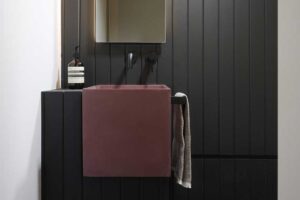 Minimalistická toaleta s tmavým dřevěným obkladem, závěsným umyvadlem v tlumeném odstínu a subtilním zrcadlem.