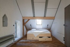 Podkrovní ložnice s vestavěnou postelí dřevěnými parketami a přiznanými trámy