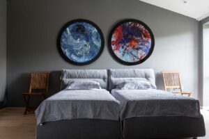 Hostovská ložnice se dvěma samostatnými lůžky, jemnými barvami a uměleckými obrazy na stěně v domě Ridnyj