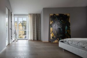 Umělecký obraz opřený o stěnu v klidné ložnici ve světlých tónech, součást osobitého interiéru domu Ridnyj