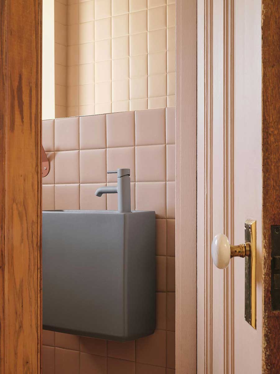 Minimalistické umyvadlo v růžové toaletě s keramickými obklady a původními dřevěnými dveřmi