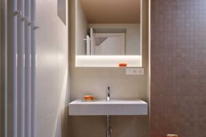 Moderní koupelna s minimalistickým umyvadlem podsvíceným zrcadlem a jemnou barevností