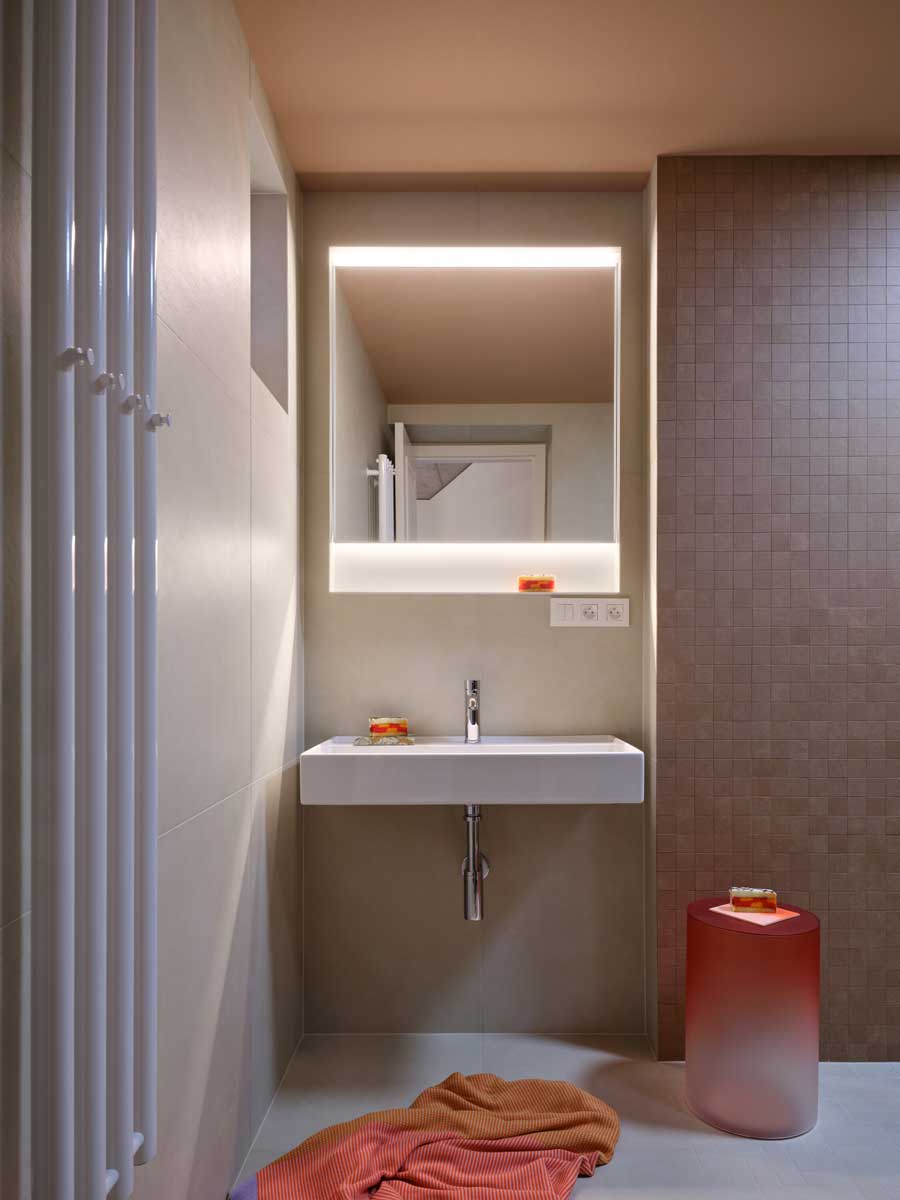 Moderní koupelna s minimalistickým umyvadlem podsvíceným zrcadlem a jemnou barevností