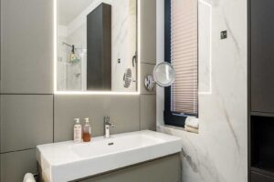 Umyvadlová skříňka se zapuštěným umyvadlem a zrcadlem s integrovaným LED podsvícením.