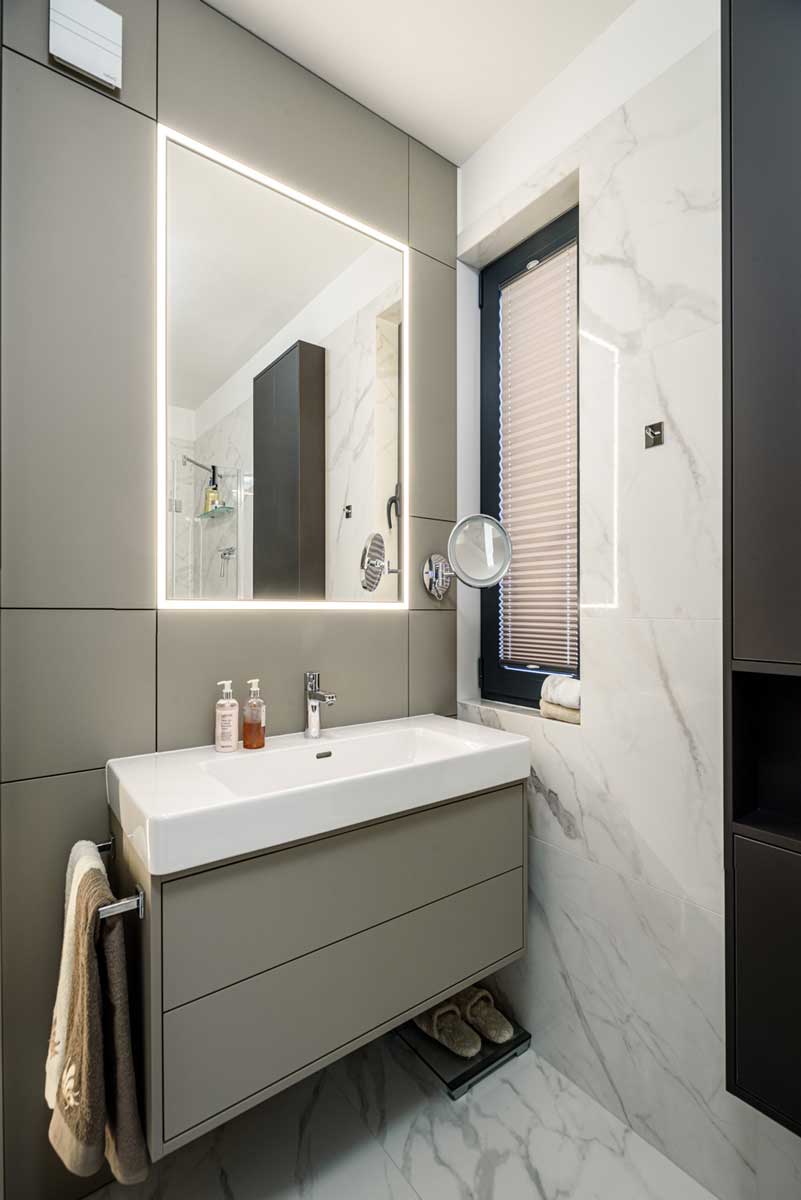 Umyvadlová skříňka se zapuštěným umyvadlem a zrcadlem s integrovaným LED podsvícením.