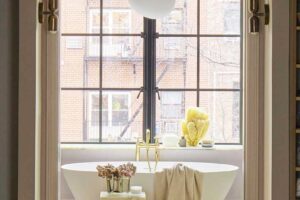 Volně stojící vana umístěná u okna s výhledem a mosaznými bateriemi