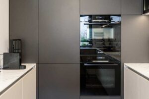 Kuchyňská stěna s vestavěnou troubou a spotřebiči integrovanými do tmavých skříní.