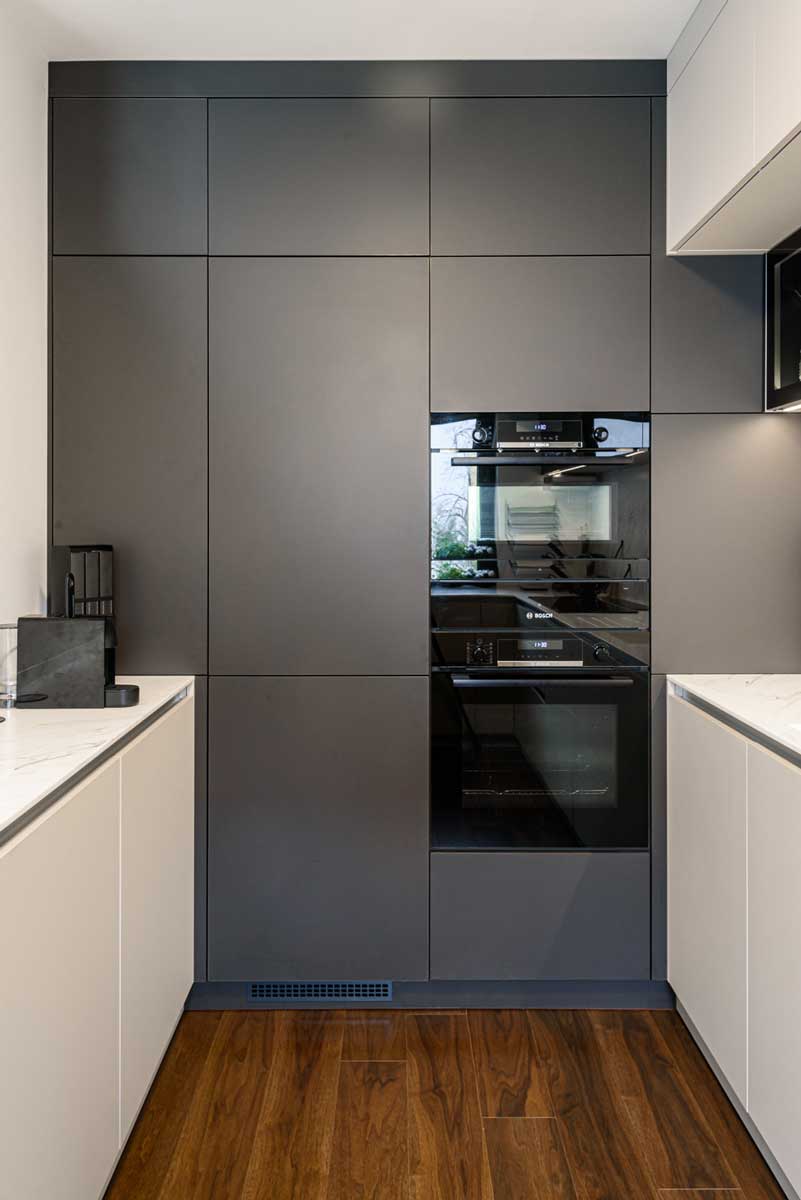 Kuchyňská stěna s vestavěnou troubou a spotřebiči integrovanými do tmavých skříní.