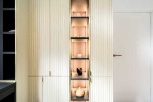 Vestavěná vitrína s vertikálním podsvícením a dekorativními policemi zapuštěnými do skříňové stěny.