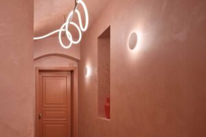 Chodba v pavlačovém domě s pudrovými omítkami kazetovými dveřmi a atypickým liniovým svítidlem