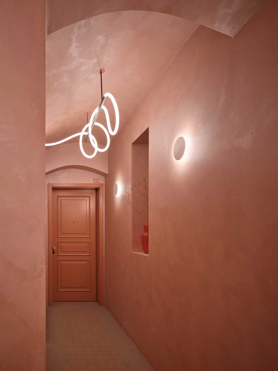 Chodba v pavlačovém domě s pudrovými omítkami kazetovými dveřmi a atypickým liniovým svítidlem