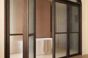 Prosklené dveře s tmavým dřevěným rámem vedoucí do koupelny v rekonstruovaném domě