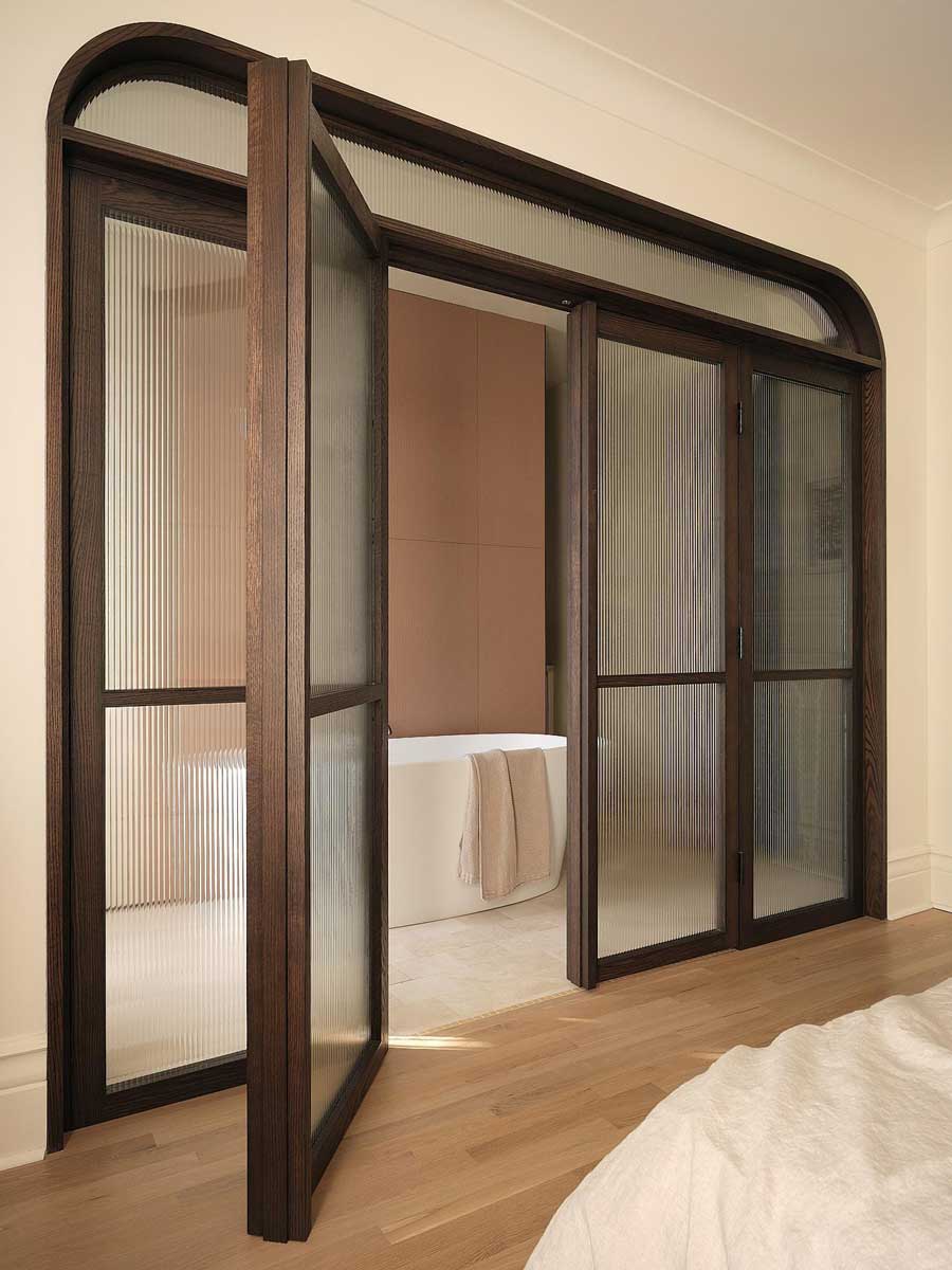 Prosklené dveře s tmavým dřevěným rámem vedoucí do koupelny v rekonstruovaném domě