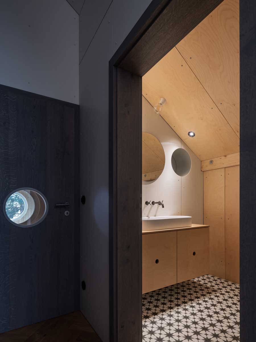 Vstup do koupelny s dřevěnými dveřmi kruhovým okénkem a světlým interiérem