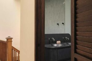 Vstup do koupelny s tmavým vestavěným umyvadlem, zaobleným průchodem a původním dřevěným schodištěm