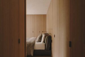 Vstup do ložnice obložený dřevem s vestavěnými skříněmi v minimalistickém interiéru rodinného domu